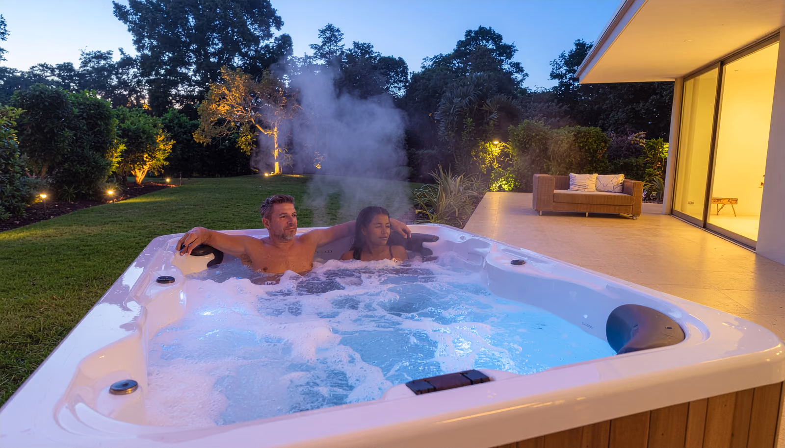 A couple relaxing together in a warm therapy spa in their backyard at dusk